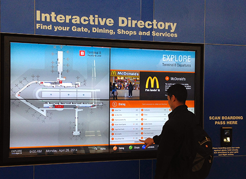 Terminal B Passenger in front of an example of the digital signage displaying the interactive terminal map and dining choices in Terminal B at Boston Logan