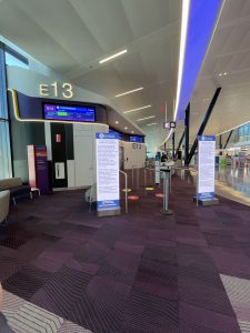 Photo of 1/2 of gate 13 at Boston Logan Terminal E showing the Gate information display screen over head and Customs and Border Protection mandated information on two LED totem signs in the foreground